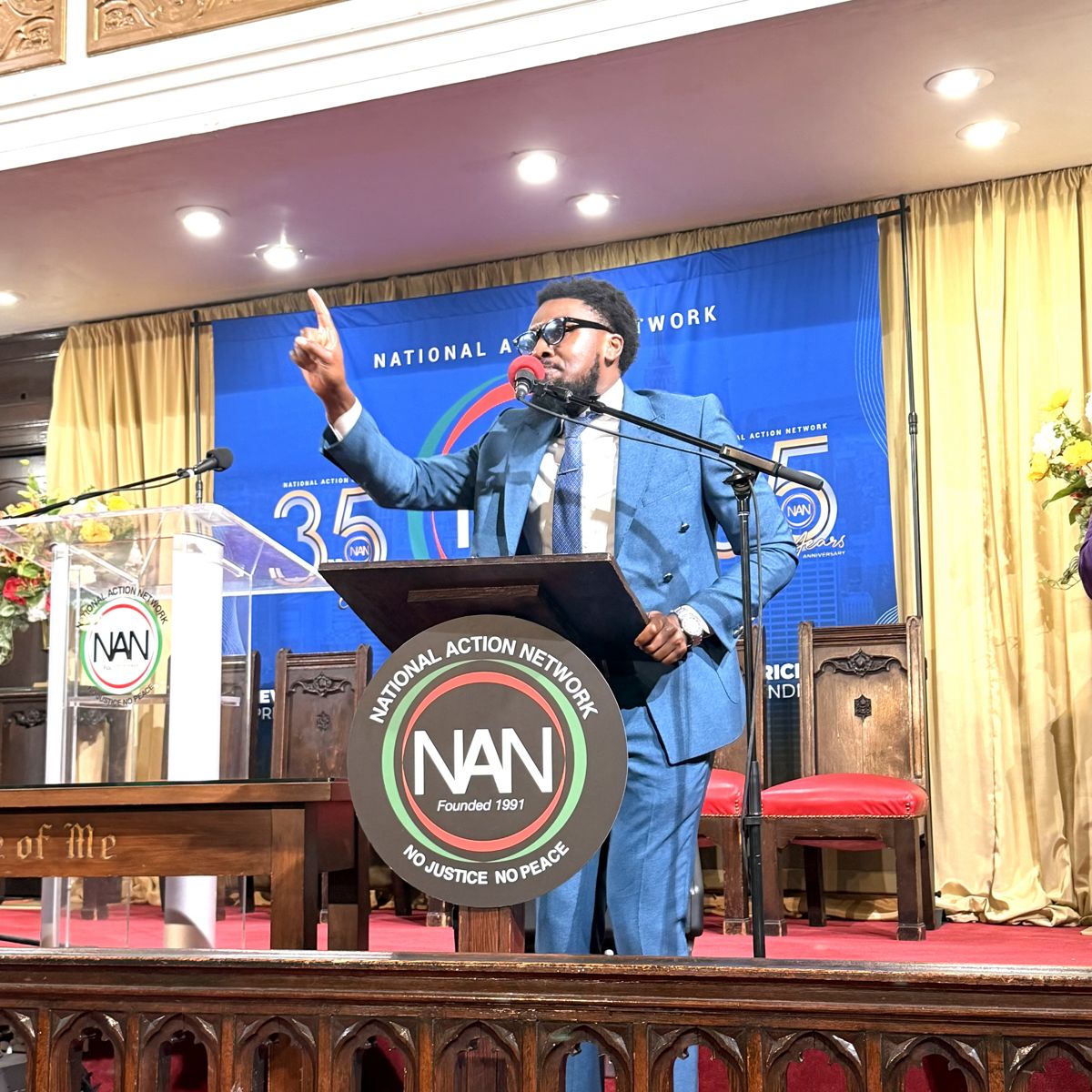 Jahleel Spence speaking from a podium at a National Action Network event